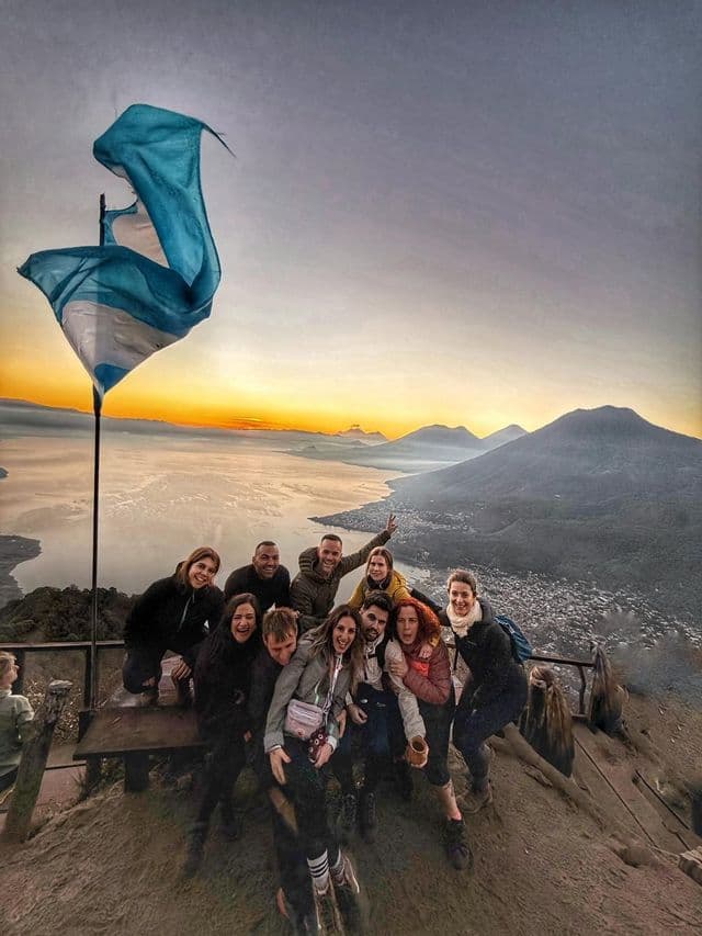 Un viaje en grupo de WeRoad posa para una foto en un mirador de montaña al amanecer, con vistas a un lago y volcanes distantes.