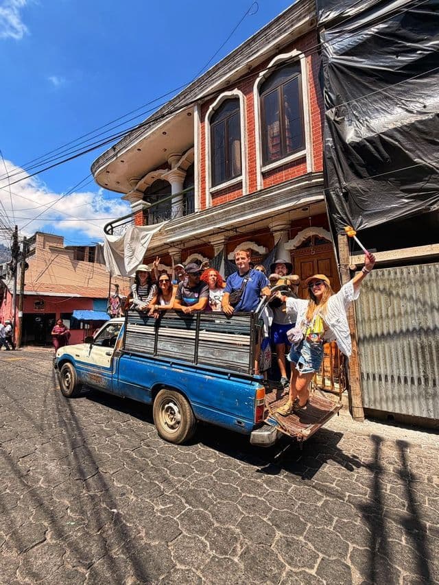 Un grupo de WeRoad en la parte trasera de una camioneta azul, recorriendo una calle empedrada estrecha en un día soleado.
