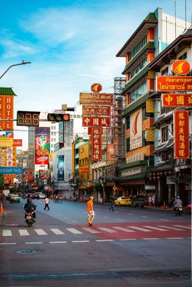 Una strada animata a Chinatown, con pedoni, traffico ed edifici colorati, ricoperti di insegne verticali, sotto un cielo azzurro e luminoso.