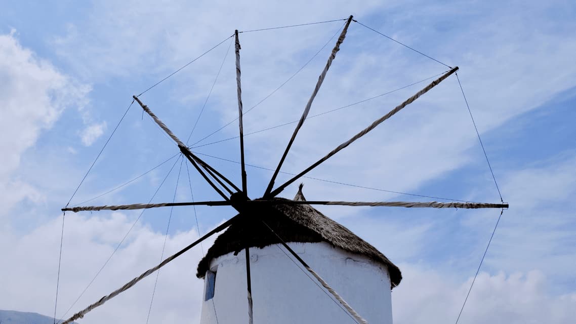 La cima di un tradizionale mulino a vento bianco con tetto di paglia e vele arrotolate contro un cielo azzurro con nuvole.