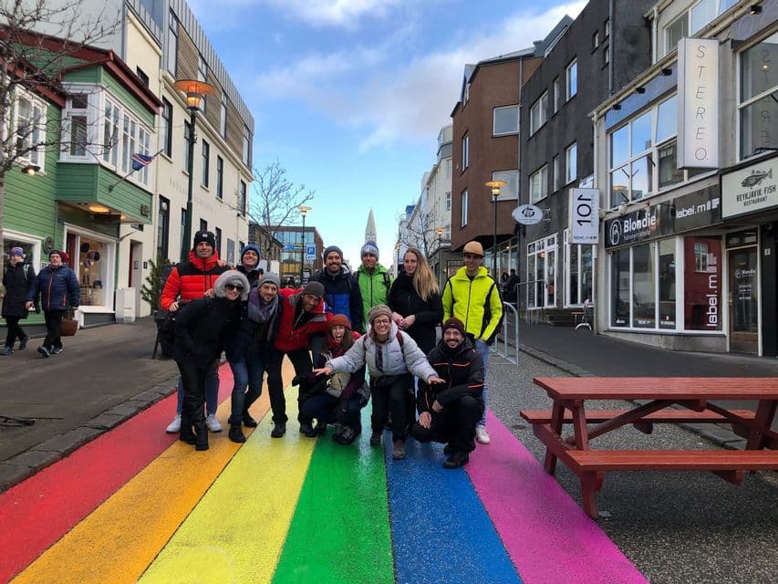 Un viaje en grupo de WeRoad posando para una foto en una calle pintada con rayas arcoíris, con edificios de la ciudad de fondo.