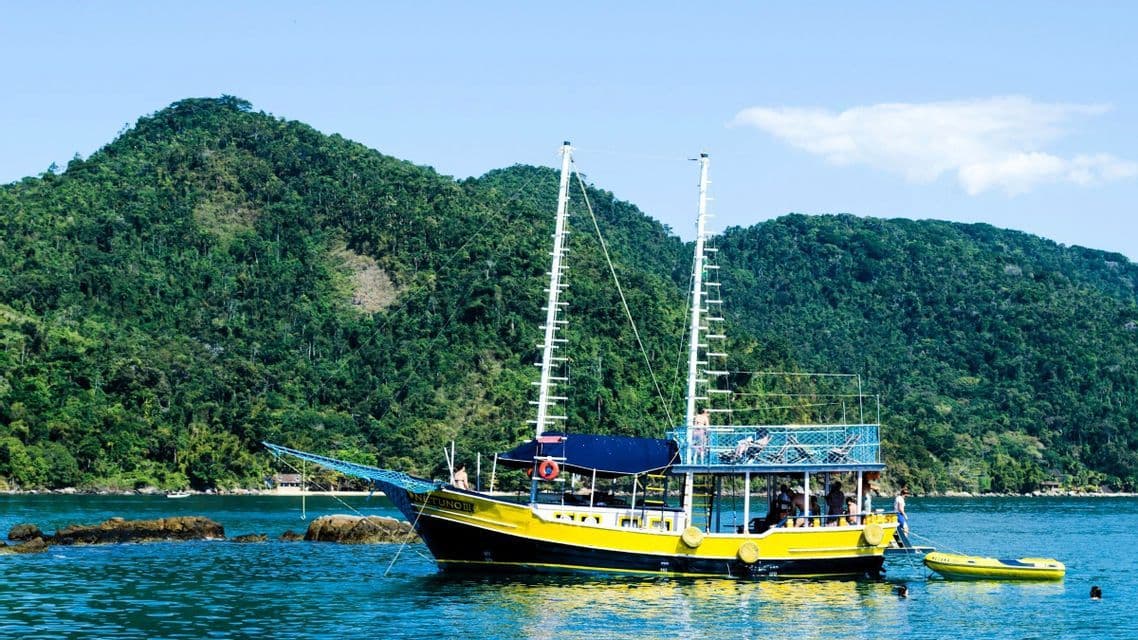 Eine WeRoad Gruppenreise auf einem gelb-schwarzen Ausflugsboot, das im Wasser vor üppigen, bewaldeten Hügeln ankert.
