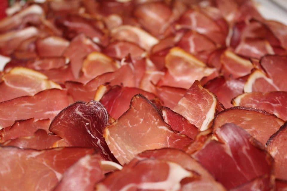 Primo piano di salumi affettati sottilmente, che mostrano il loro colore rosso e le venature di grasso bianco, disposti a strati sovrapposti.