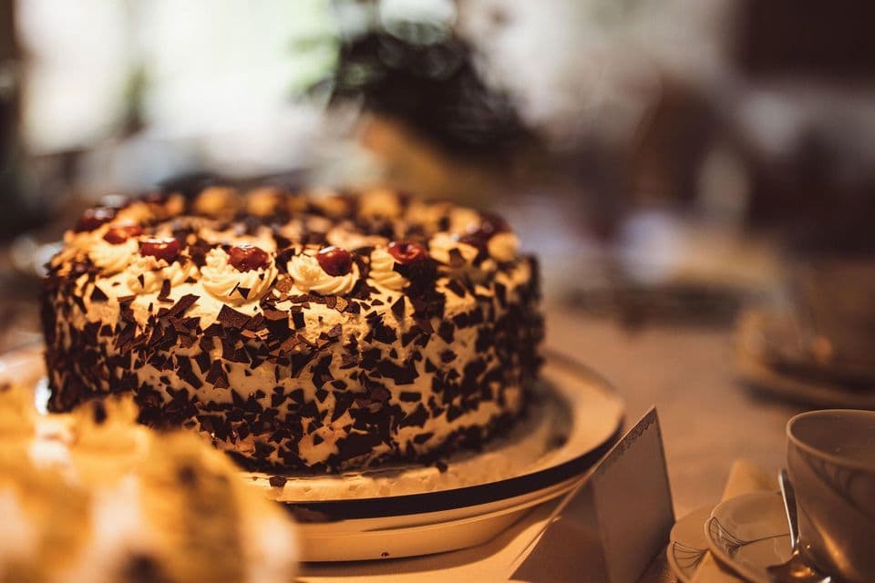 Una torta della Foresta Nera, guarnita con scaglie di cioccolato, panna montata e ciliegie, è adagiata su un piatto.