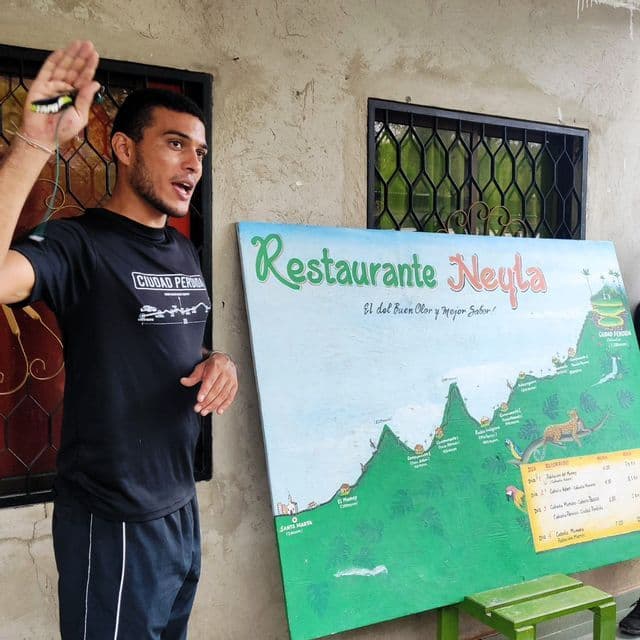 Ein Reiseführer im 'Ciudad Perdida'-T-Shirt gestikuliert und erklärt eine Wanderung auf einer großen, illustrierten Karte.
