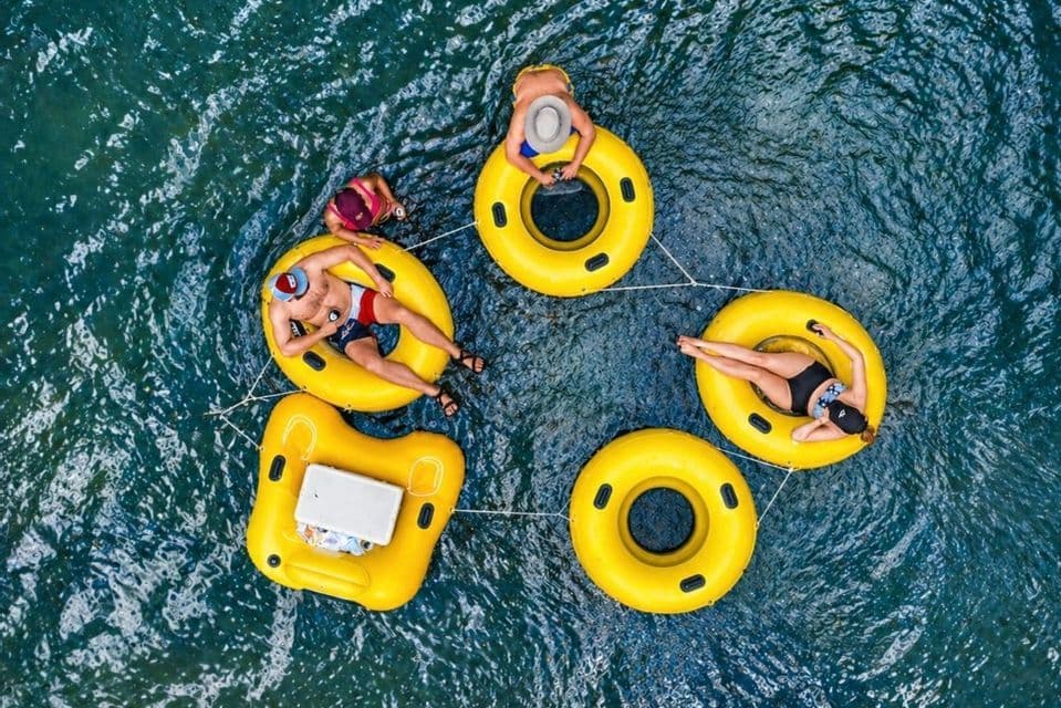 An aerial view of a WeRoad group trip relaxing in yellow inflatable rings tied together on blue water.