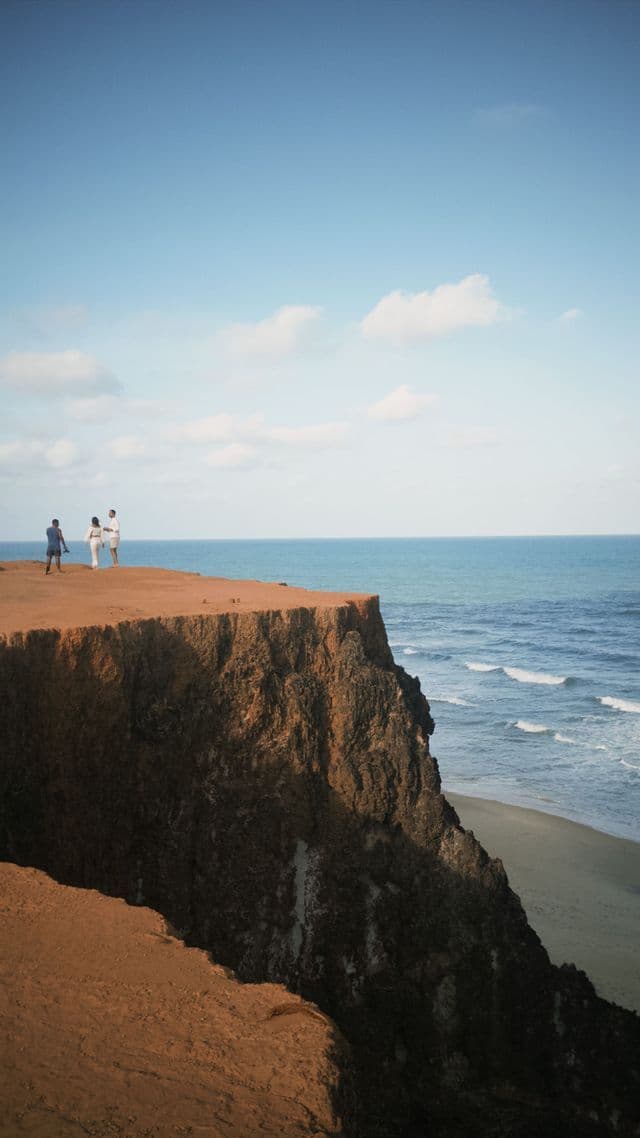 Tre persone di un gruppo WeRoad sono in piedi su un'alta scogliera di terra rossa, ammirando l'oceano.