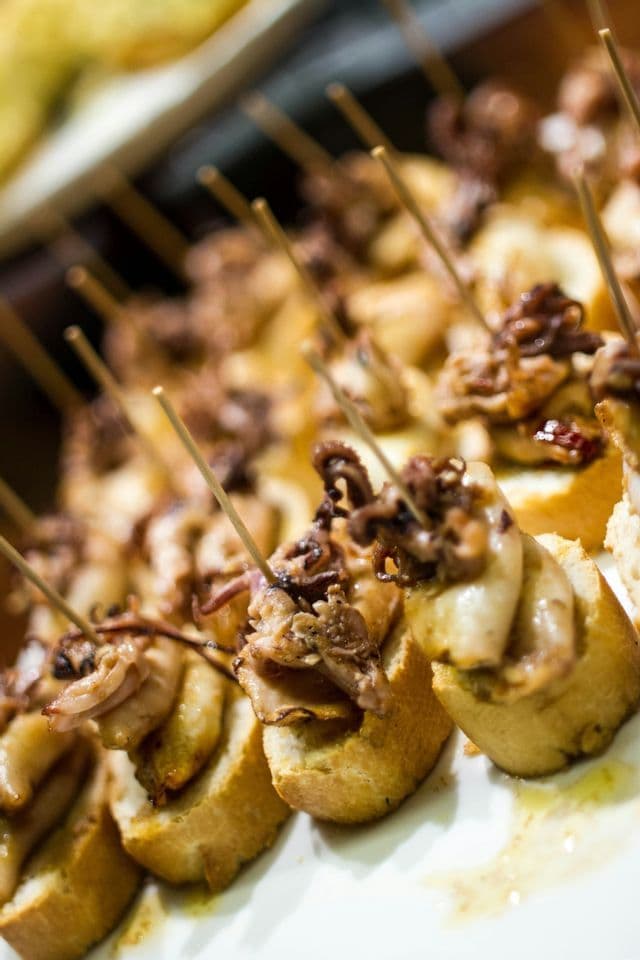 A close-up of octopus pintxos with toothpicks, arranged in rows on a white plate, with a shallow depth of field.