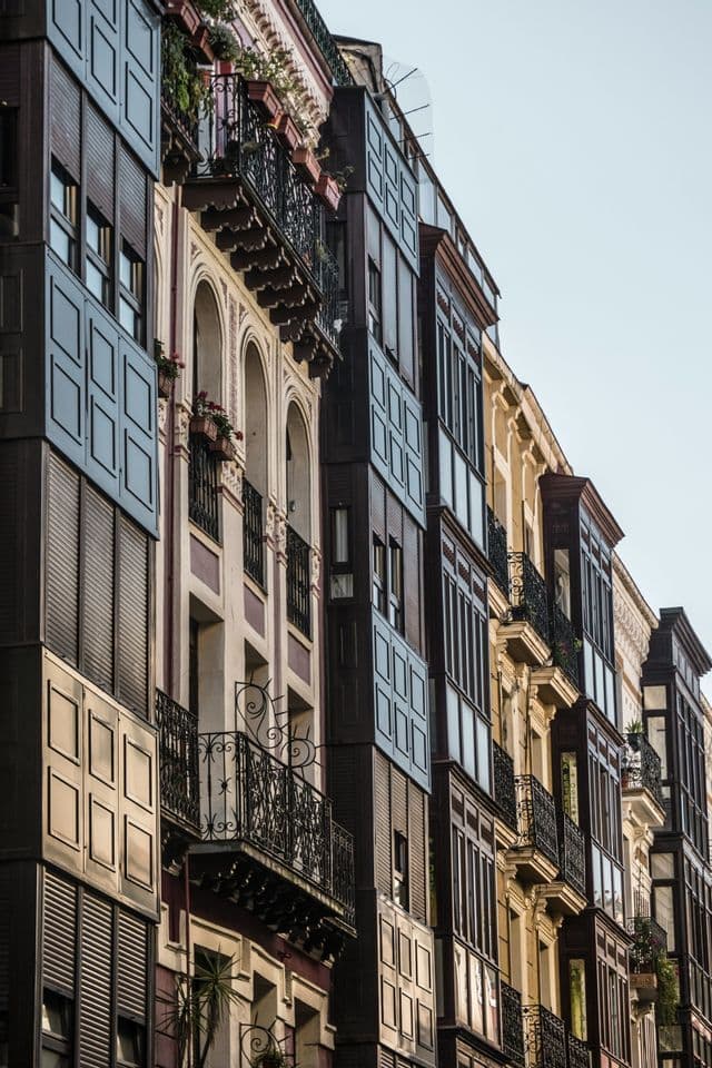 A row of ornate buildings with varied facades, featuring enclosed glass balconies and decorative wrought-iron railings.