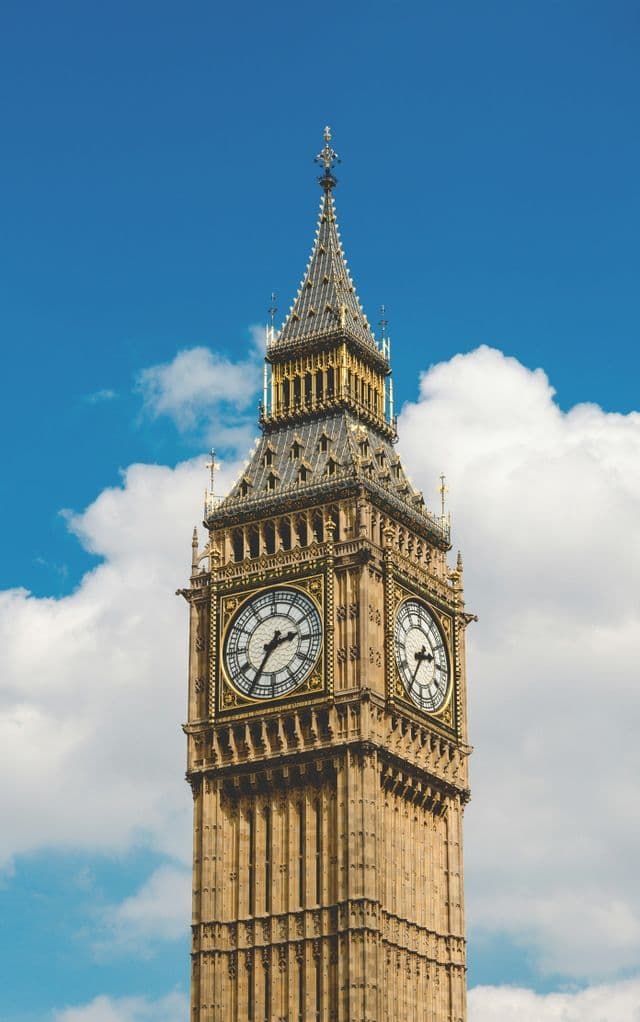 The ornate clock tower, Big Ben, seen from a low angle against a blue sky with white clouds.