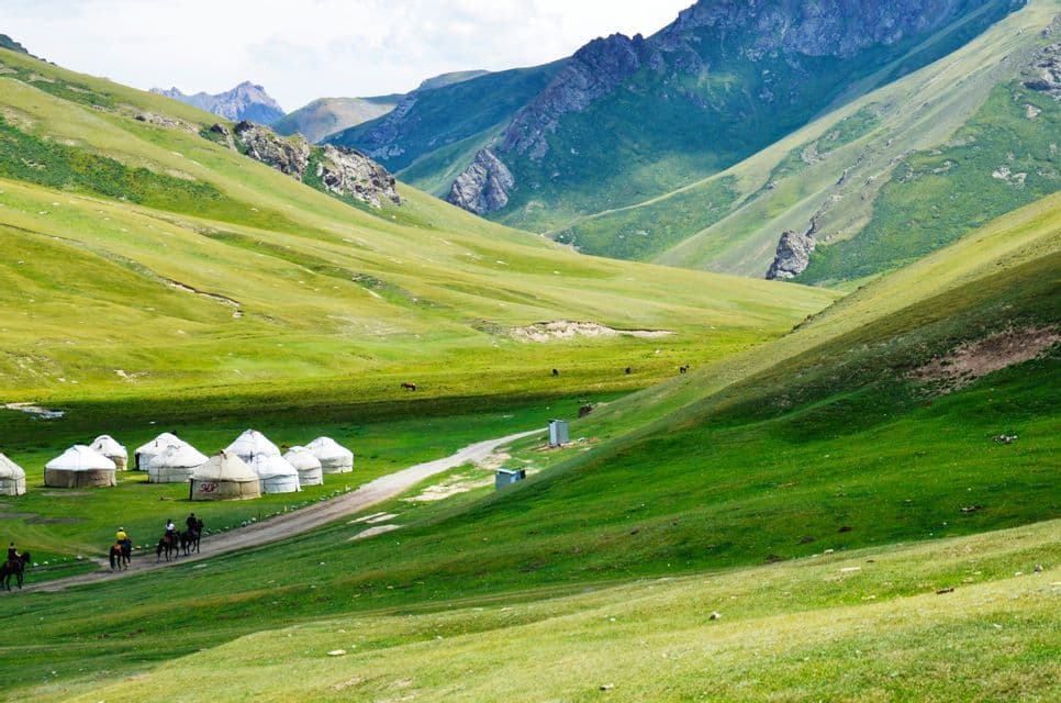 Un voyage de groupe WeRoad à cheval, traversant une vaste vallée de montagne verdoyante et passant devant un camp de yourtes.