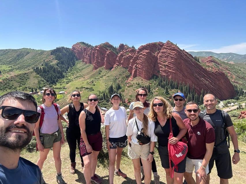 Un groupe WeRoad en voyage prend un selfie devant une chaîne de montagnes rocheuses rouges par une journée ensoleillée.