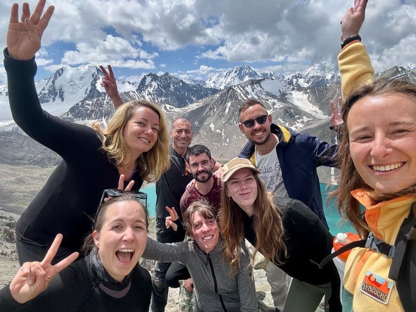 Un groupe WeRoad en voyage prend un selfie devant des montagnes enneigées et un lac alpin turquoise.
