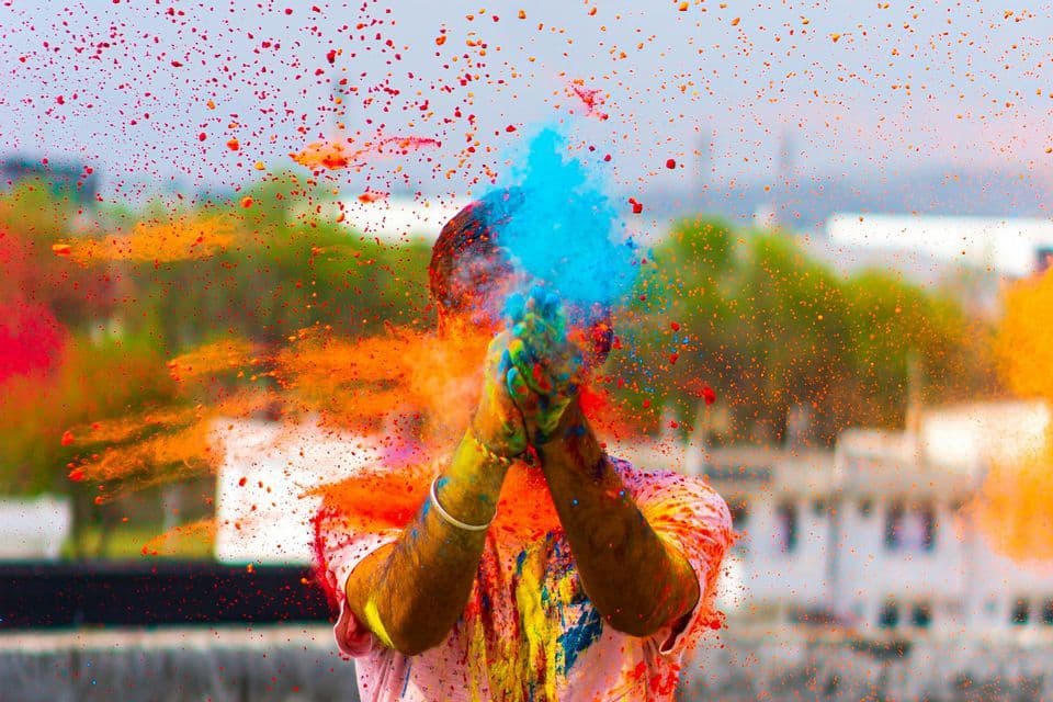 Una persona batte le mani, provocando un'esplosione di polvere colorata blu, arancione e rossa nell'aria.