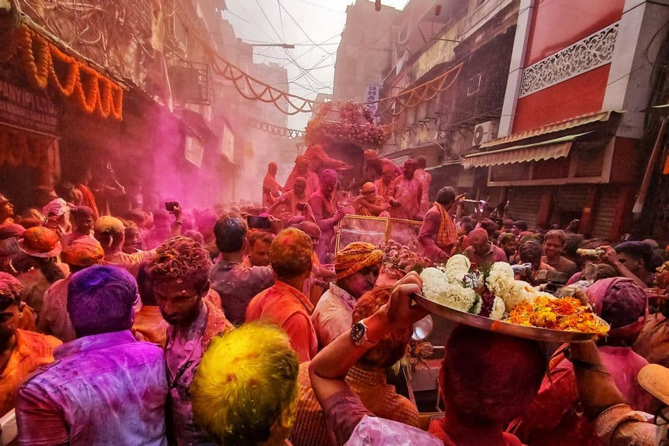 Una fitta folla di persone coperte di polveri colorate celebra il festival Holi in una stretta strada decorata.