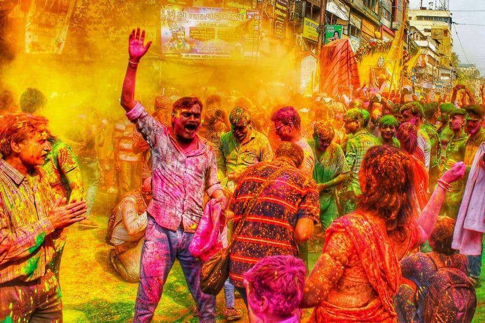 Una folla di persone celebra il festival Holi per strada, con i corpi e i vestiti coperti di polveri colorate.
