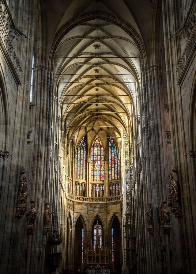 L'intérieur d'une cathédrale gothique, avec son haut plafond voûté, de hautes colonnes de pierre et un grand vitrail coloré.
