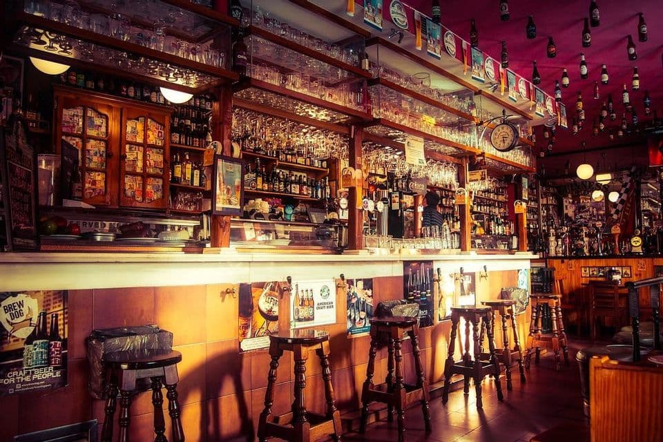 Intérieur chaleureux d'un pub classique vide, avec un bar en bois bien garni, des tabourets et des verres suspendus au-dessus.