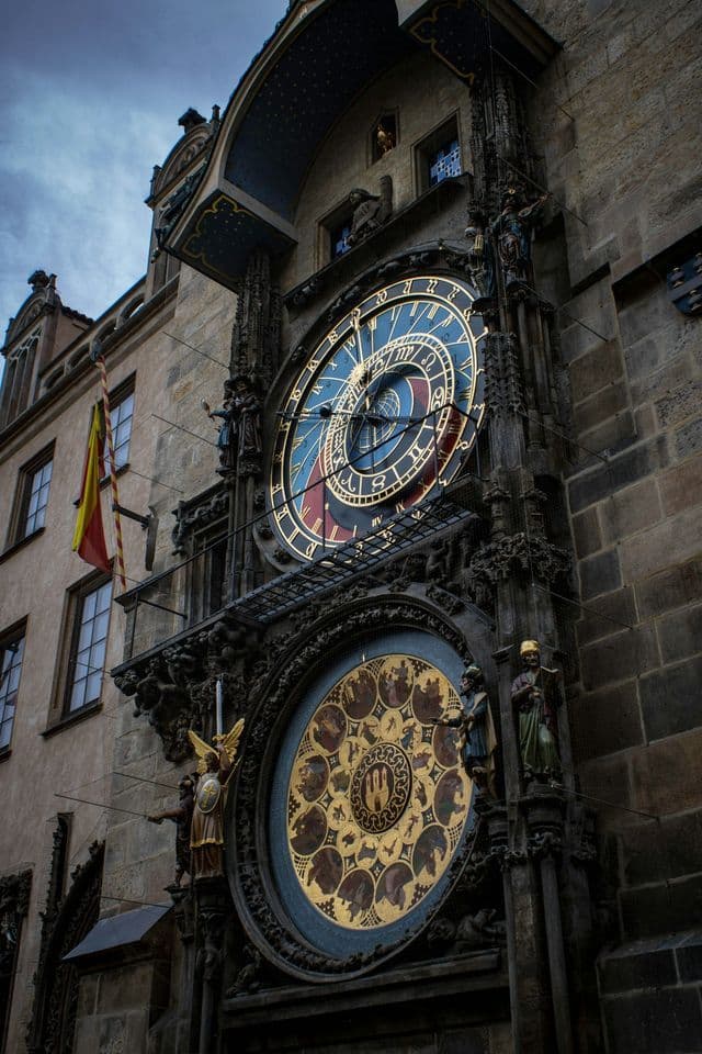 Une vue en contre-plongée d'une grande horloge astronomique ornée avec des cadrans bleus et dorés, montée sur la façade d'un bâtiment en pierre.