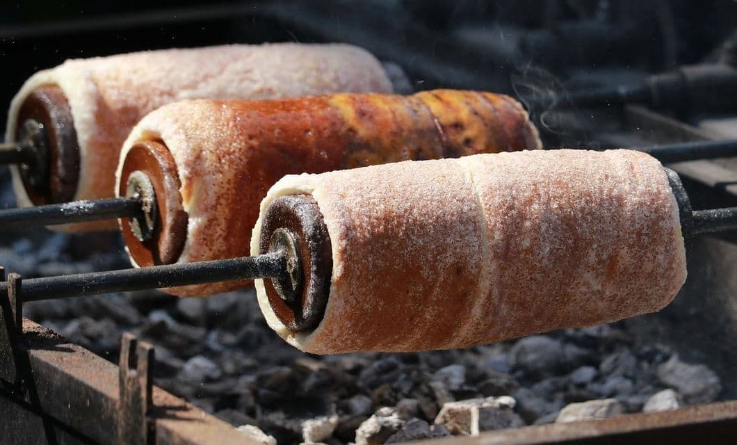 Trois gâteaux cheminée rôtissant sur des broches tournantes au-dessus de braises ardentes, avec de la vapeur s'élevant.