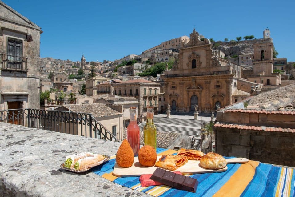 A spread of traditional pastries and food on a stone balcony overlooking a historic hillside town with a large church.