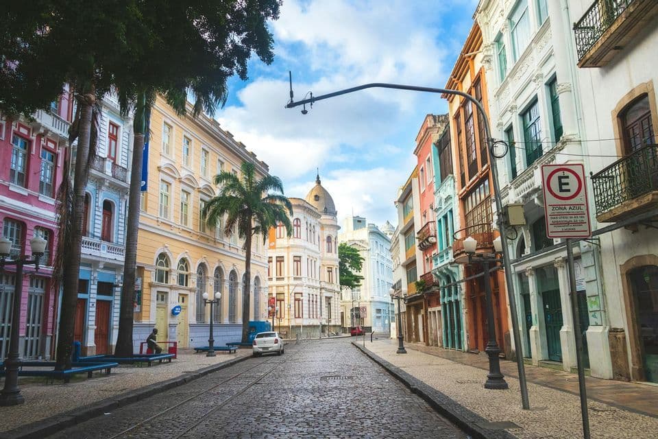 Una strada acciottolata con binari del tram è fiancheggiata da edifici colorati in stile coloniale e palme sotto un cielo azzurro.