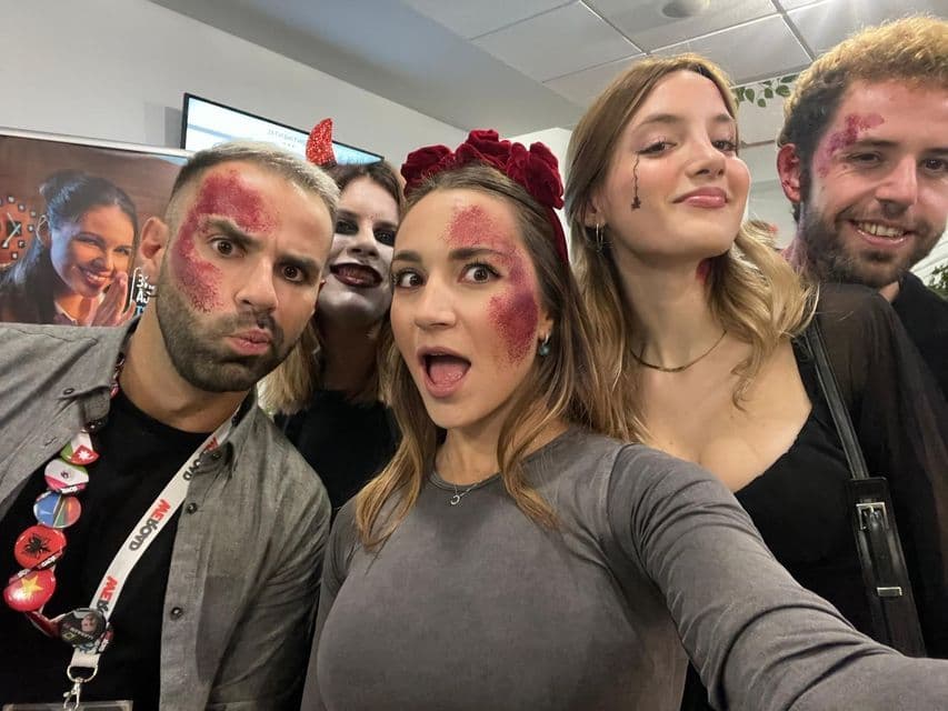 Un gruppo di cinque persone con trucco e costumi di Halloween con glitter rossi in posa per un selfie al chiuso.