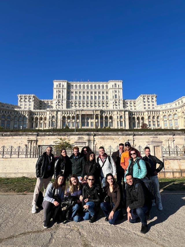 Un gruppo WeRoad in viaggio posa per una foto davanti a un maestoso edificio storico sotto un cielo azzurro e limpido.