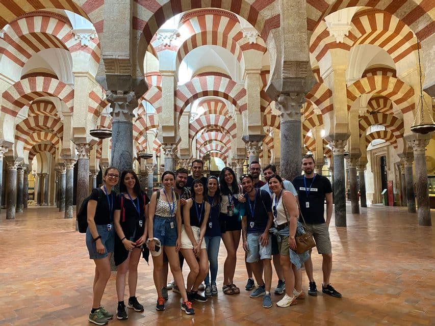 Eine WeRoad-Gruppenreise posiert für ein Foto in einer großen Halle mit markanten rot-weiß gestreiften Bögen und Säulen.
