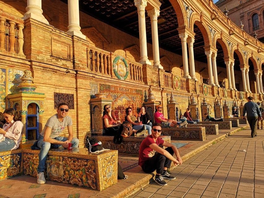 Un voyage de groupe WeRoad se détendant sur des bancs carrelés ornés devant un bâtiment en arcades à l'heure dorée.