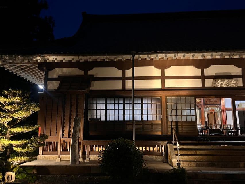 Un tempio tradizionale giapponese con architettura in legno è illuminato di notte, le sue finestre a griglia che brillano contro il cielo scuro.