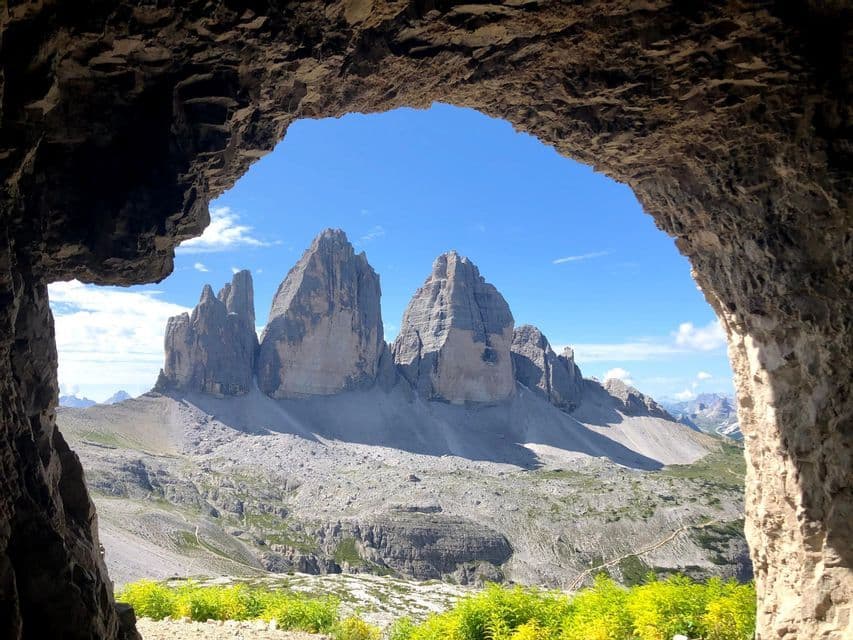 A view of a jagged mountain range with rocky slopes, framed by the entrance of a dark cave under a clear blue sky.