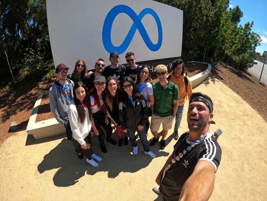 Eine WeRoad-Gruppenreise macht an einem sonnigen Tag ein Selfie und lächelt gemeinsam vor dem großen Outdoor-Meta-Logo-Schild.