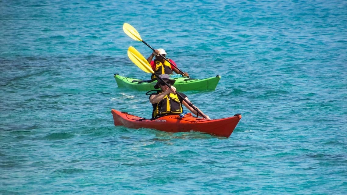 Due persone in un viaggio di gruppo WeRoad remano con kayak arancione e verde su acque turchesi.