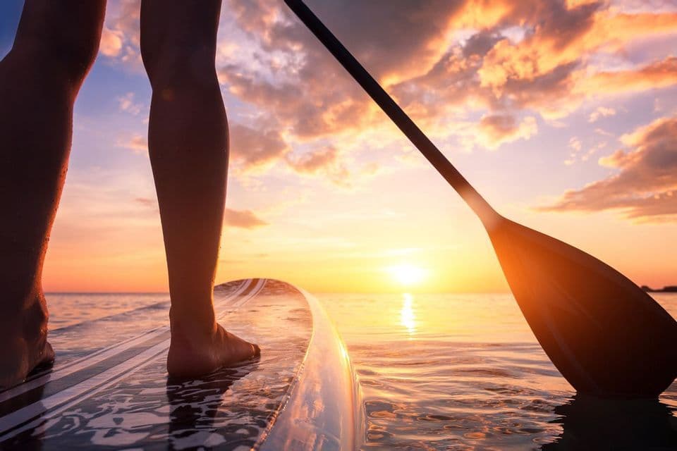 Gambe su SUP al tramonto sull'acqua.
