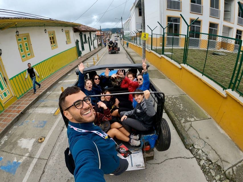 Un hombre se toma una selfie sonriendo con un grupo de viaje WeRoad en la parte trasera de un vehículo descapotable en una calle de la ciudad.