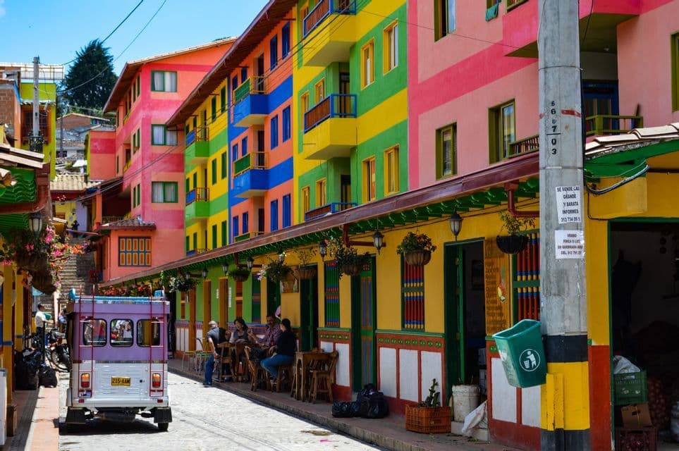 Una strada acciottolata è fiancheggiata da edifici dai colori vivaci dipinti a strisce orizzontali, con un piccolo veicolo parcheggiato a lato.