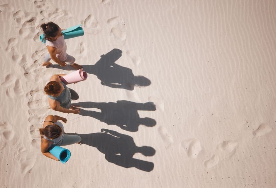 Draufsicht auf eine WeRoad-Gruppe, die über Sand läuft, bunte Yogamatten trägt und lange Schatten wirft.