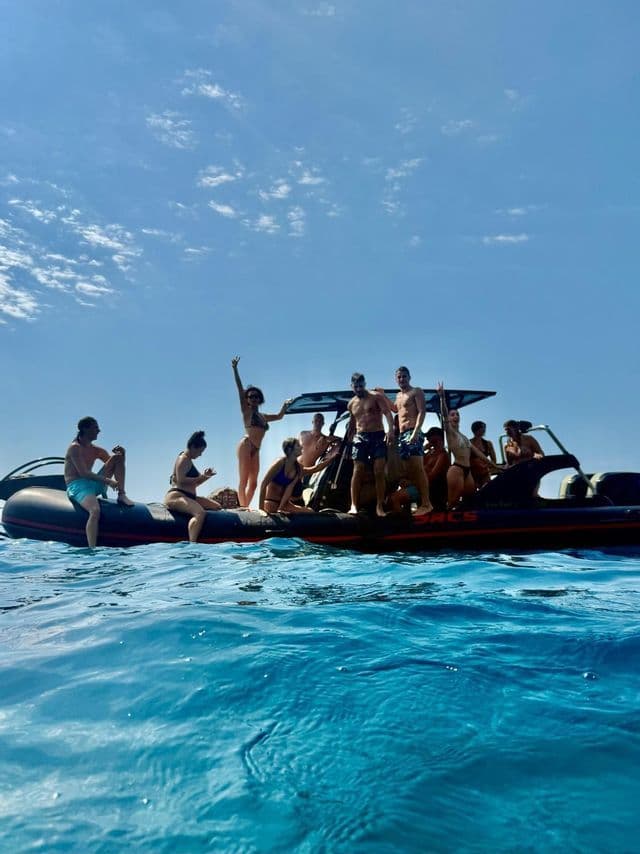 Un gruppo WeRoad in costume da bagno posa su un gommone in mezzo al mare blu.