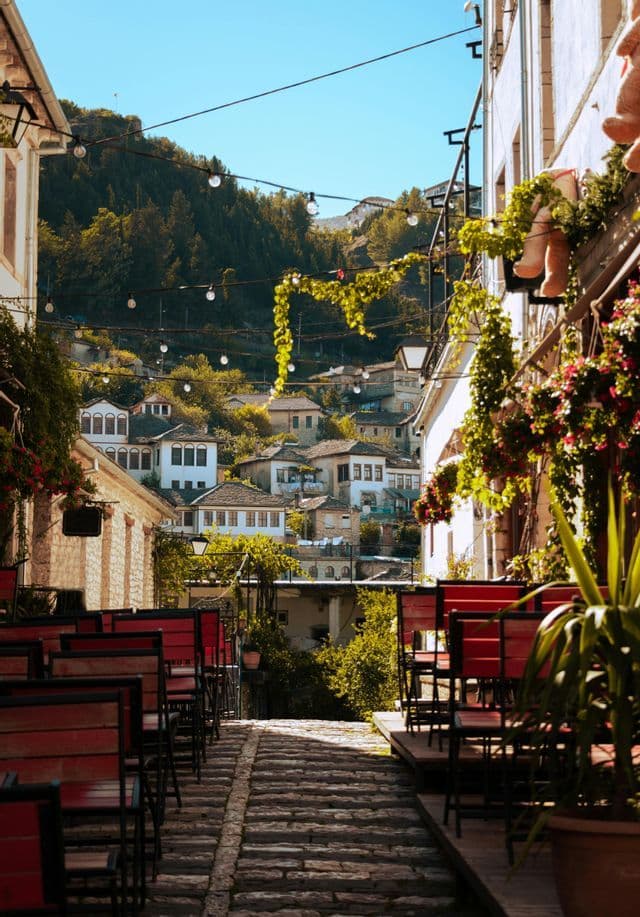 Una stretta via acciottolata si snoda attraverso un borgo collinare, costeggiata da tavolini di caffè all'aperto e lucine.