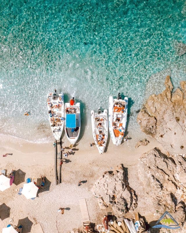 Una vista aerea dall'alto di un viaggio di gruppo WeRoad su barche ormeggiate a una spiaggia sabbiosa accanto ad acqua turchese cristallina.