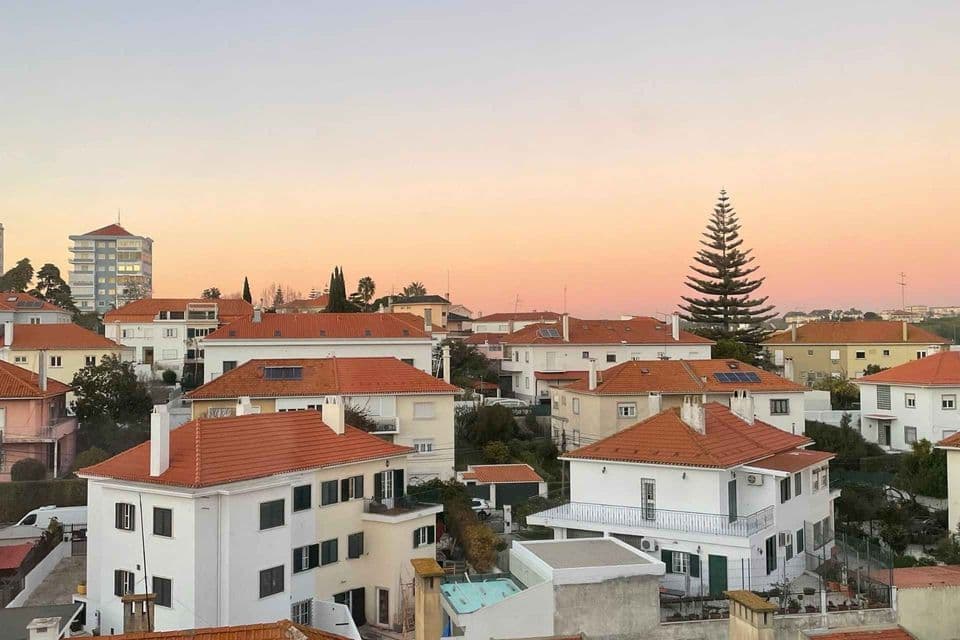 Una veduta dall'alto di un quartiere con case bianche e tetti di tegole rosse sotto un cielo al tramonto dai colori pastello.