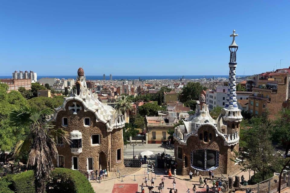 Una veduta dall'alto di due edifici con mosaici in un parco, con un ampio paesaggio urbano e il mare sullo sfondo.
