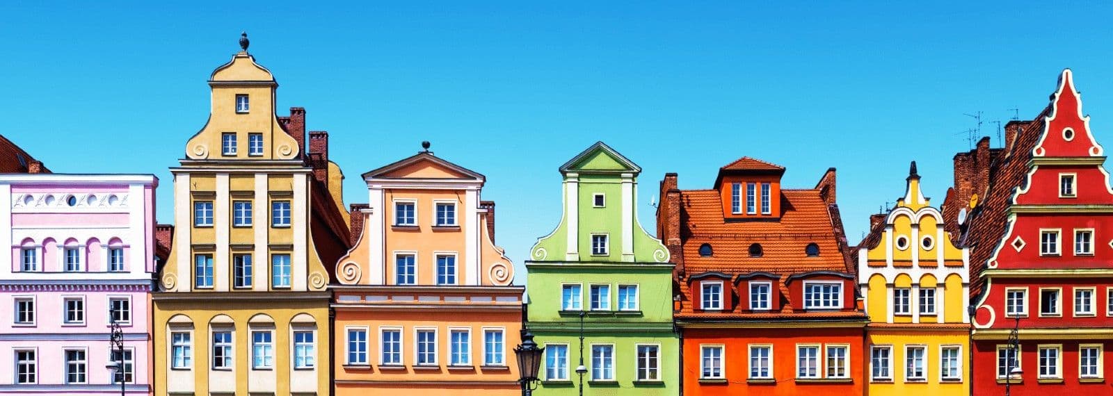 Una fila di edifici dai colori vivaci con frontoni decorati si staglia contro un cielo azzurro e limpido.