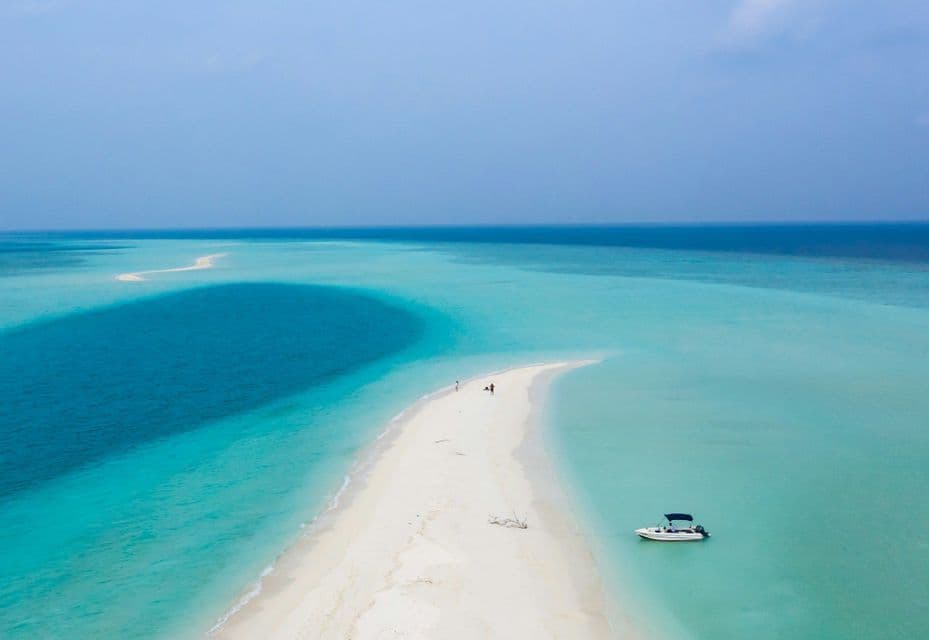 Vista aerea di un banco di sabbia bianco che si protende nell'oceano turchese e blu intenso, con una piccola imbarcazione ormeggiata nelle vicinanze.