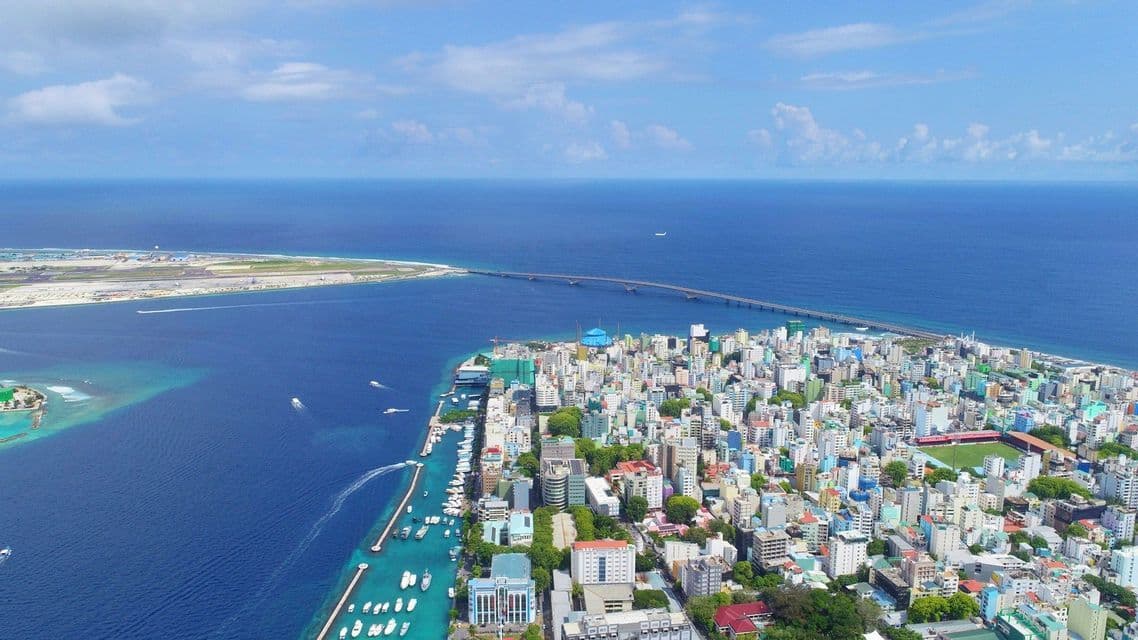 Una vista aerea di una città densamente popolata su un'isola, circondata da un oceano blu profondo con un lungo ponte che la collega a un'altra isola.
