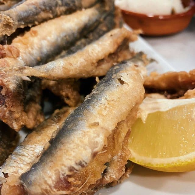 Primo piano di un piatto di pesciolini fritti dorati, serviti con uno spicchio di limone e una piccola ciotola di salsa d'accompagnamento.