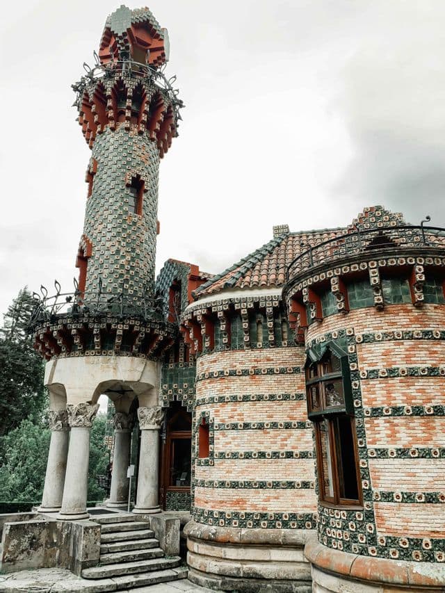 Un edificio sontuoso con un'alta torre e mura curve in mattoni, decorate con piastrelle verdi e rosse, sotto un cielo nuvoloso.