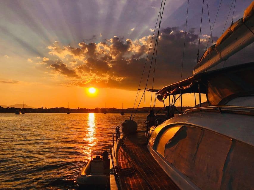 Blick von einem Segelboot auf einen goldenen Sonnenuntergang über dem Wasser, mit Sonnenstrahlen, die durch die Wolken brechen.