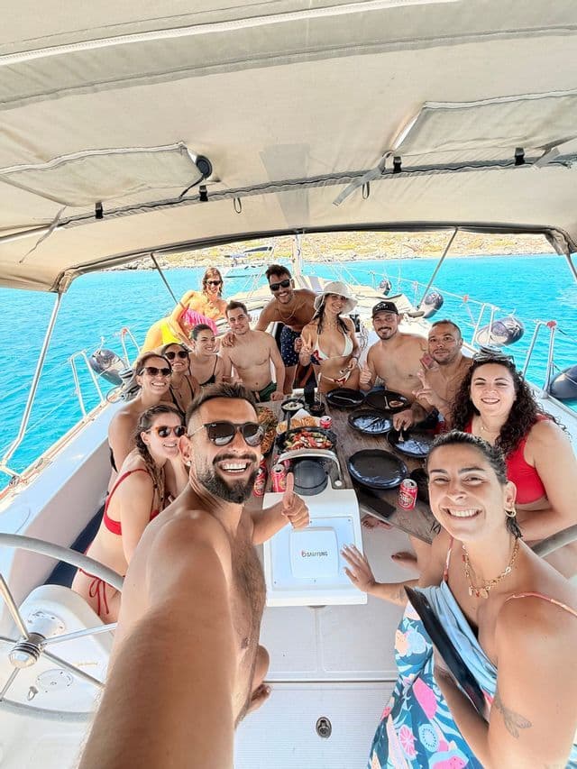 Eine WeRoad Gruppe macht auf einem Segelboot ein Selfie auf offener See, umgeben von Essen und Getränken an einem Tisch.